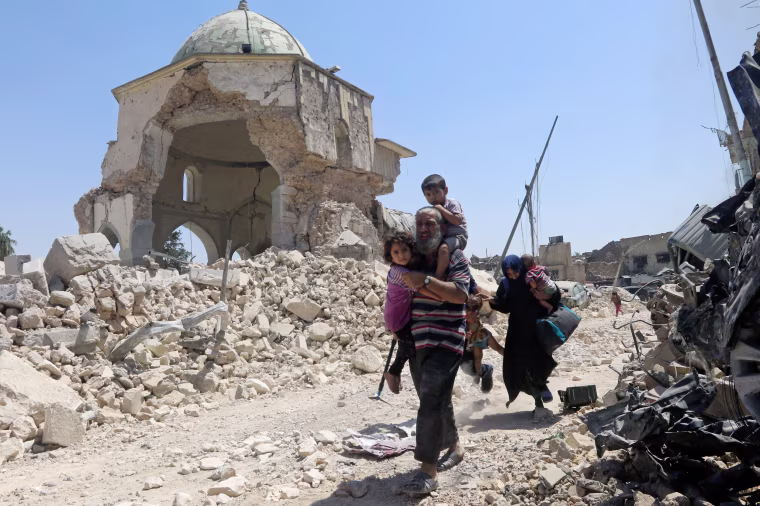 Image: Displaced Iraqi civilians walk past the ruined Grand al-Nuri Mosque after fleeing their homes on June 30.