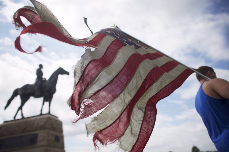 Image: William Gillis carries a tattered flag besides a battlefield monument as activists gather at the Gettysburg National Military Park