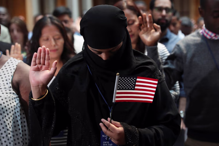 Image: Immigrants hold their hands up during the Pledge of Allegiance at a U.S. Citizenship and Immigration Services Naturalization ceremony in the New York Public Library in New York