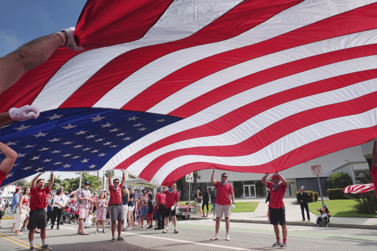 Image: Participants carry an American flag during the 4th of July parade in Santa Monica