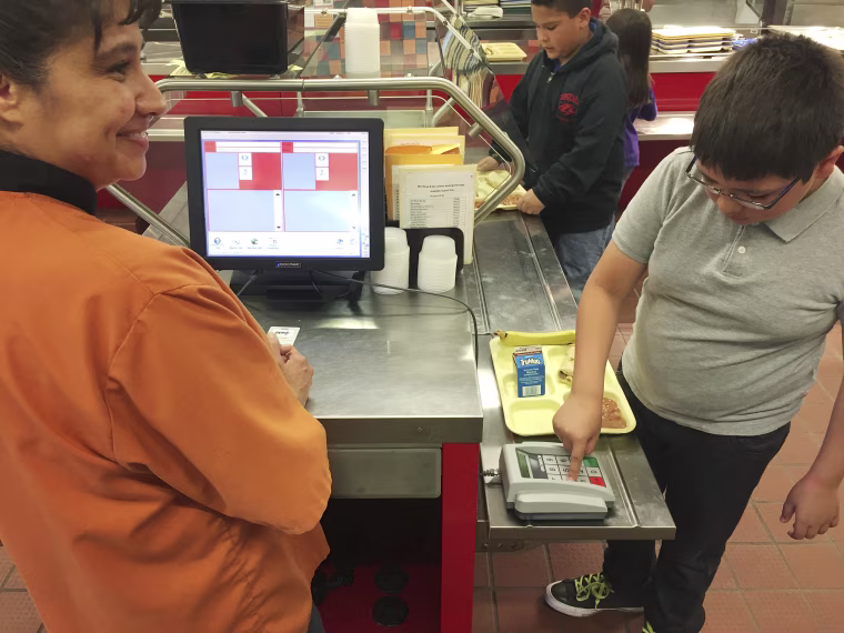 Image: Cafeteria worker Paula Herrera, left, supervises as second grade student Dylan Casias punches in his student identification number