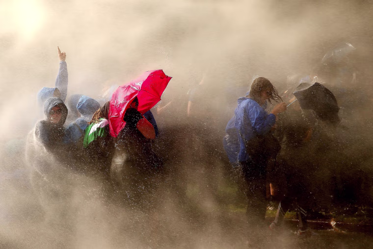 Image: Demonstrators are hit by water cannons of the police as they protest