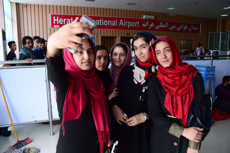 Image: Afghan teenagers from the Afghanistan Robotic House take pictures with a mobile phone at Herat International Airport.