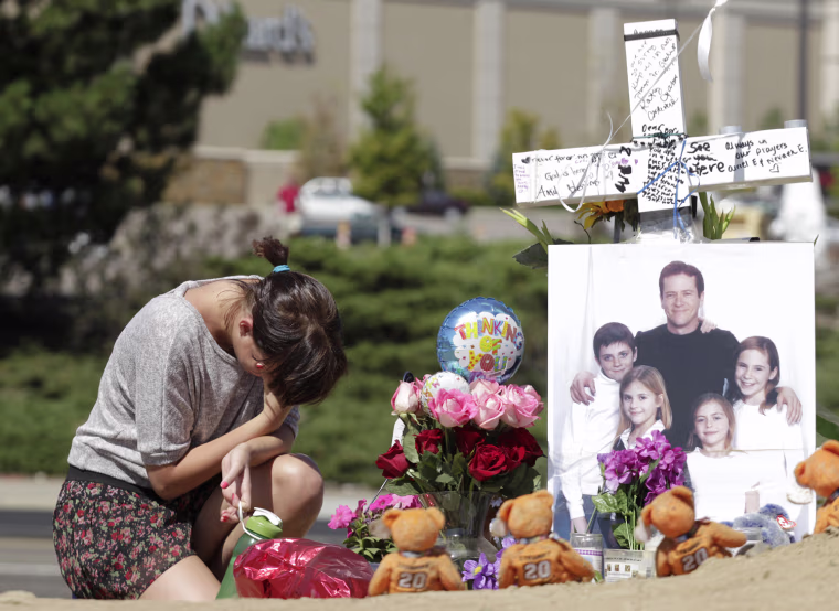 Image: Ashley Deuell, kneels next to a cross and a family photo of Gordon Cowden