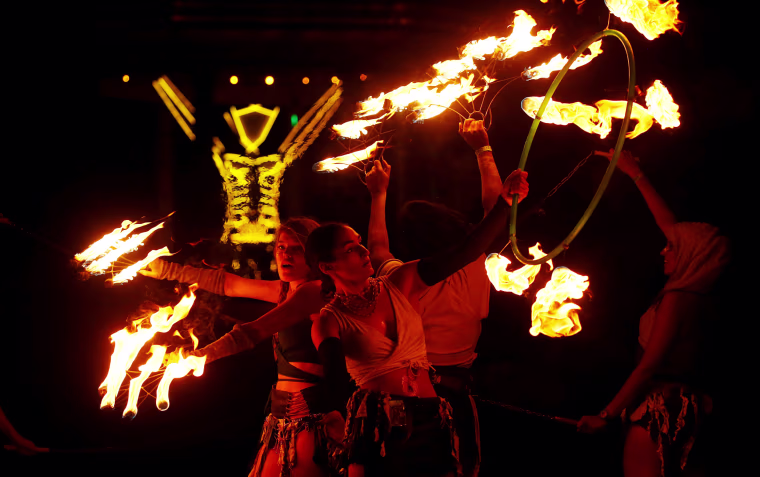 Image: Burning Man participants from the \"Revolutionary Motion\" fire conclave spin fire in front of the effigy of \"The Man\" just before the effigy is burned at the culmination of the annual Burning Man arts and music festival in the Black Rock desert of N
