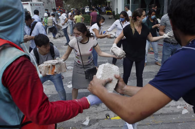 Image: Volunteers pick up the rubble from a building that collapsed