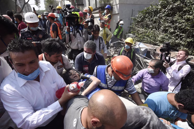 Image: A woman is carried away after being pulled out of the rubble in Mexico City