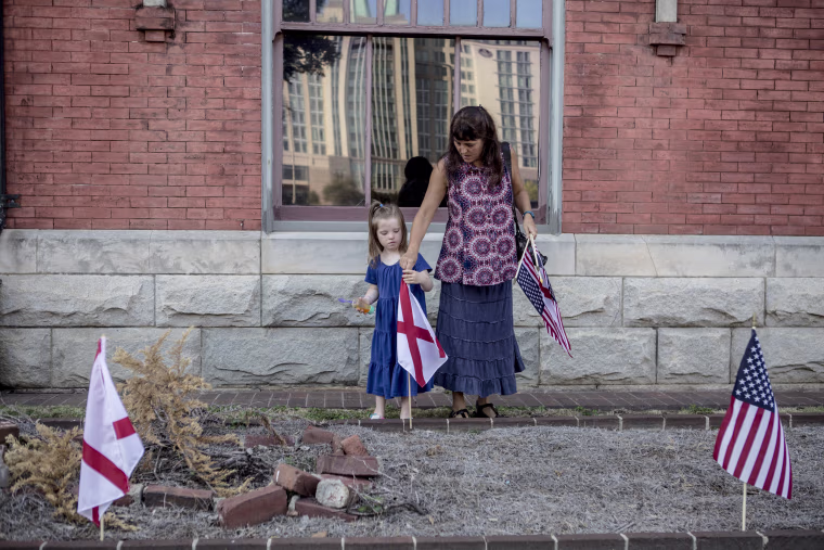 Image: Leigh Ford and her daughter Lydia, 5, plant American and state of Alabama flags outside of Train Depot.