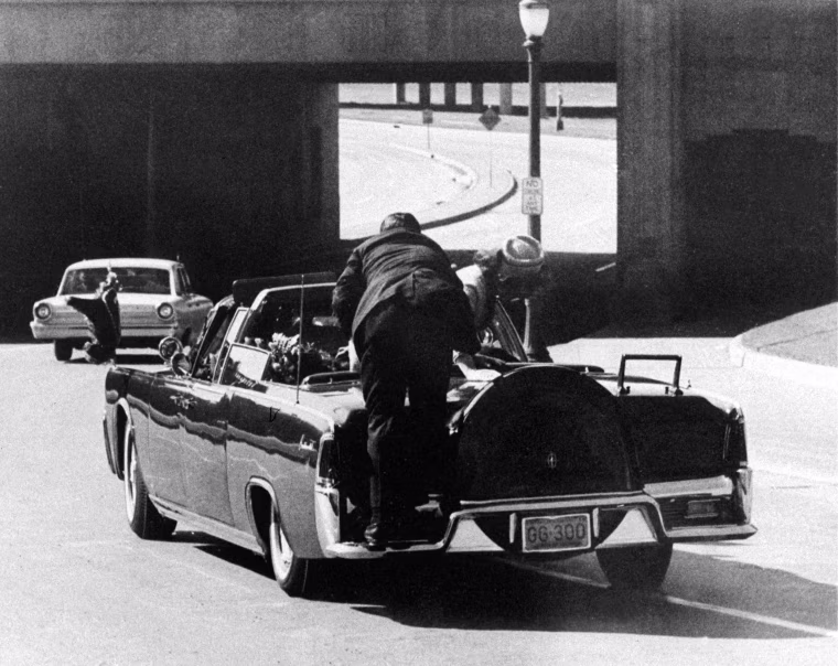 Image: President John F. Kennedy slumps down in the back seat of the Presidential limousine as it speeds along Elm Street toward the Stemmons Freeway overpass