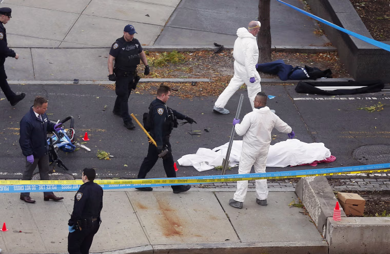 Image: Authorities investigate the scene near a covered body on a bike path