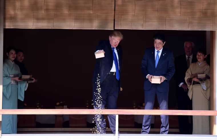 Image: After Prime Minister Abe turned his box of fish food, gently pouring the rest of its contents into the water, President Trump followed suit, slightly more abruptly dumping the remaining food into the pond.