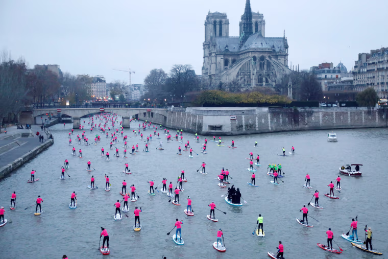 Image: Participants take part in the 8th Edition of the Nautic SUP Paris Crossing stand up paddle competition near the Notre Dame Cathedral on the river Seine in Paris