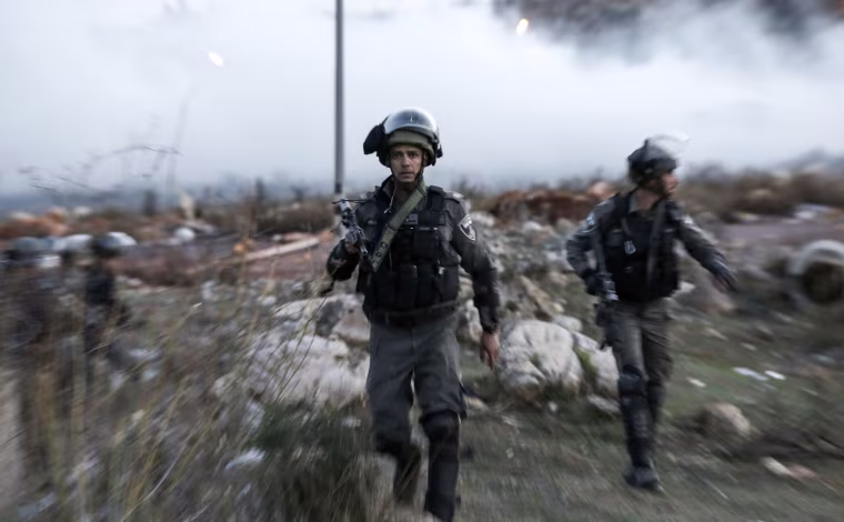 Image: An Israeli border policeman looks on as he walks through tear gas fumes during clashes with Palestinian protesters