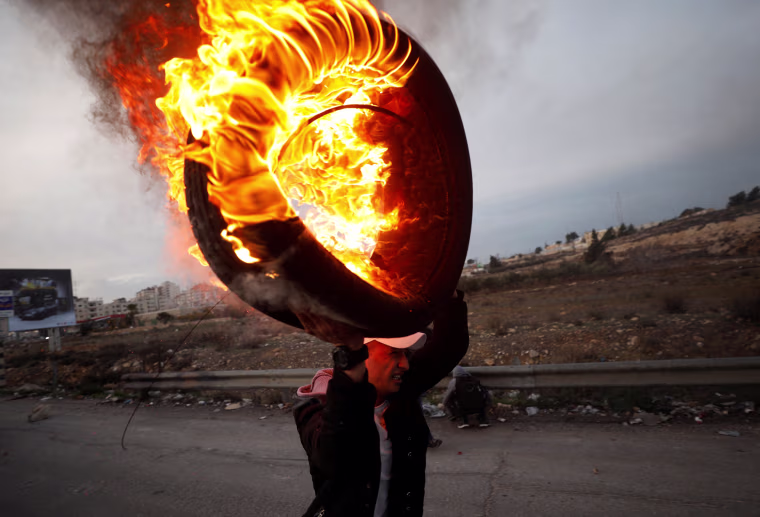 Image: A Palestinian holds a burning tire during clashes with Israeli troops near the Jewish settlement of Beit El, near Ramallah