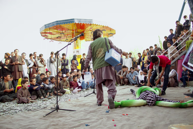 Hamid, clutching his precious box of vaccinations, attacks a snake that represents polio during the performance. The crowd cheers. "Vaccinating your children will destroy this disease!" cries Hamid. "Make sure your whole village takes these droplets and you will see how strong your children can be."