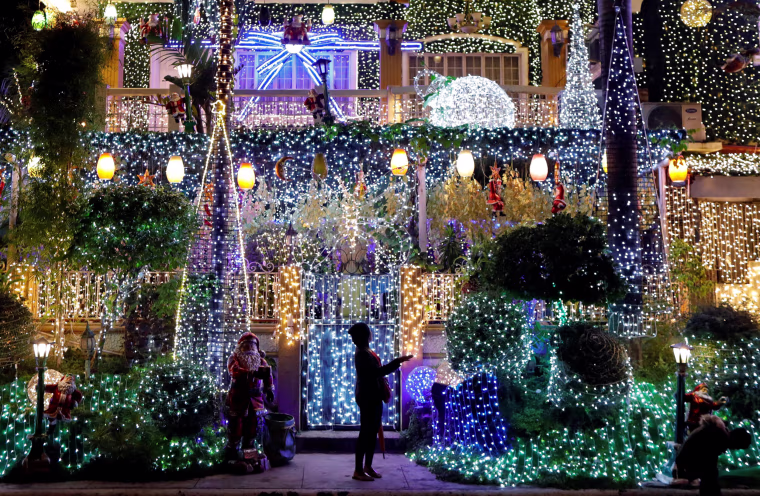 Image: A woman stands outside of a house lit up by christmas light installations in Rizal