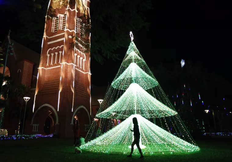 Image: A girl walks past a lit Christmas tree at Holy Trinity Cathedral in Yangon