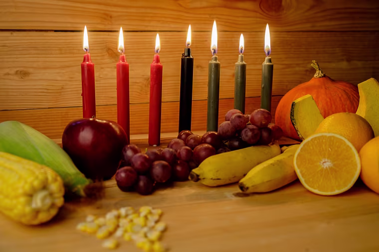 Kwanzaa holiday concept with decorate seven candles red, black and green, gift box, pumpkin,corn and fruit on wooden desk and background.