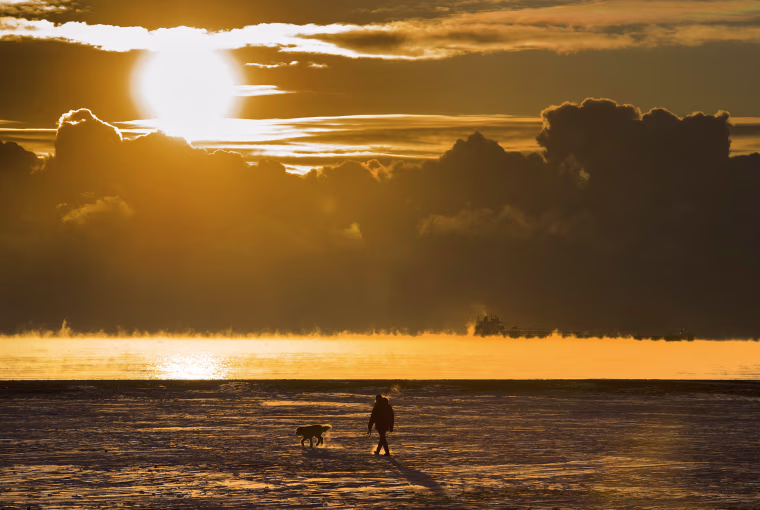 Image: A man walks his dog across the snow covered beach