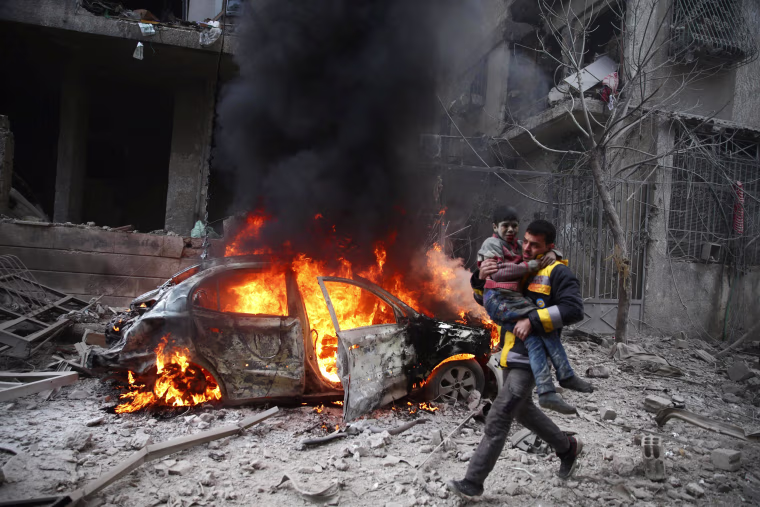 Image: A Syria Civil Defense member carries a wounded child in the besieged town of Hamouriyeh