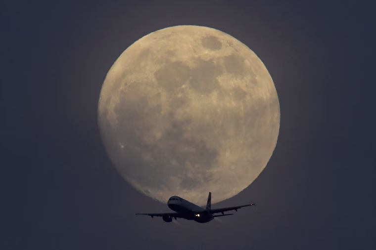 Image: A British Airways aicraft flies infront of a full moon over London