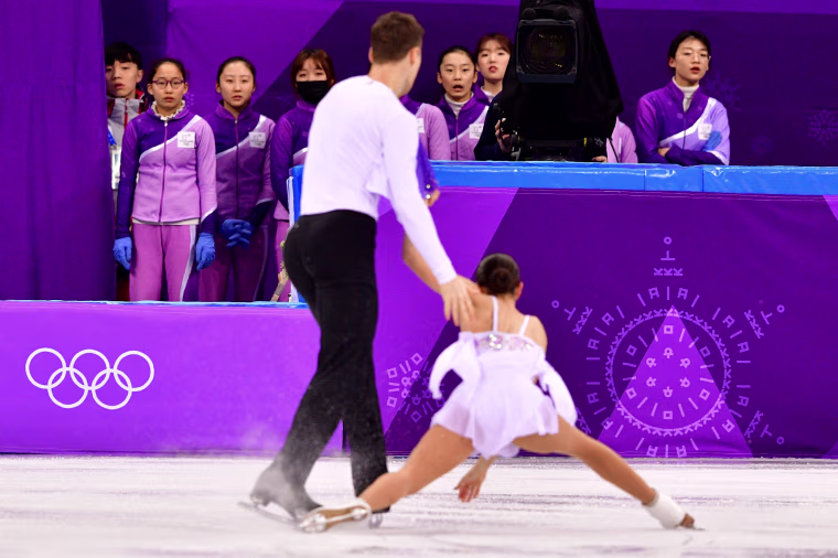 Volunteers watch as Russia's Natalia Zabiiako and Alexander Enbert compete in the figure skating team event pair skating free skating on Feb. 11.