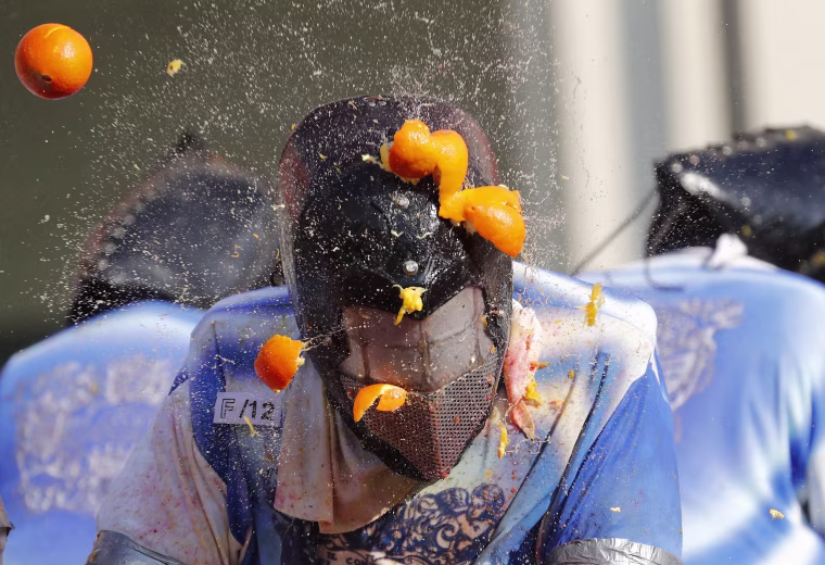 A person wearing a protection helmet is pelted with oranges during Carnival celebrations in Ivrea, Italy on Feb. 12, 2018.