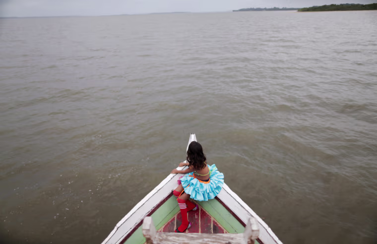 A member of the \"Bloco Real Folia\" group sits in front of a boat during Carnival of the Waters where colorful boats navigate the Jaituba river around the islands near the city of Cameta, Brazil on Feb. 9, 2018.