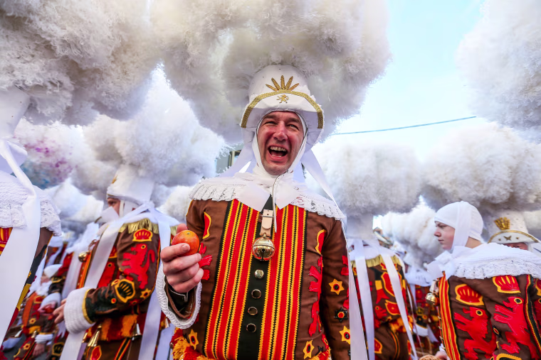 Image: Festival participant known as \"Gilles\" throw oranges during Carnival celebrations in the streets of Binche