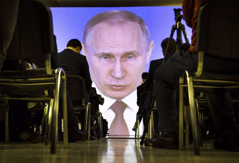 Image: Journalists watch as Russian President Vladimir Putin gives his annual state of the nation address in Moscow