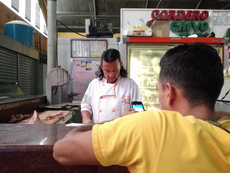 Ruben Sosa, behind the counter, helps a customer at the meat department of a Caracas supermarket.