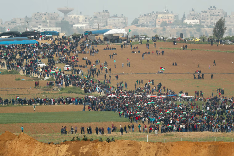 Palestinians participate in the tent city protest commemorating Land Day, with Israeli soldiers watching from across the border.