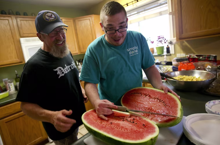 Cameron Raps, right, reacts after cutting open a watermelon beside Jeff Pool during a QueerMeals gathering