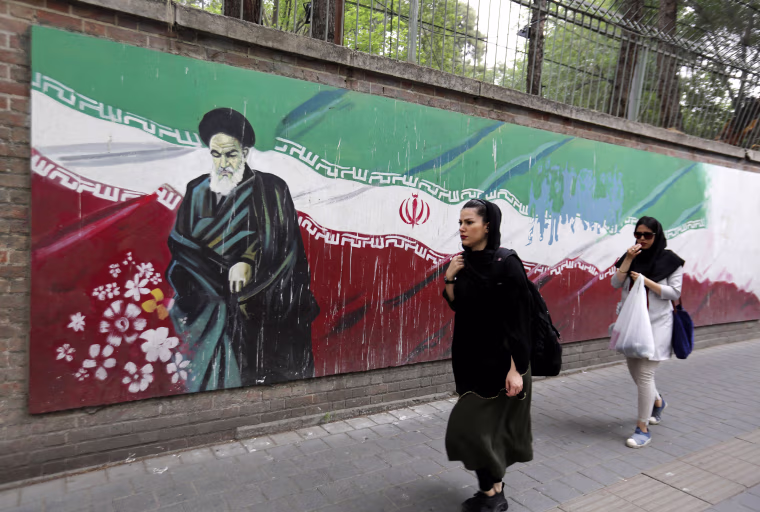 Image: An Iranian woman walks past a mural in Tehran