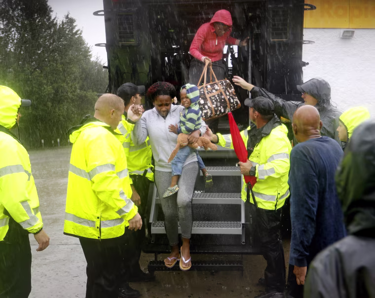 Image: Residents step out of a high water vehicle after being evacuated by the police when their neighborhood began to flood
