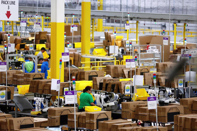 Image: Employees work at pack stations at the Amazon fulfillment center in Kent