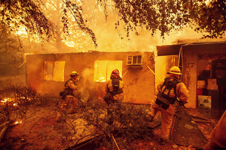 Image: Firefighters push down a wall while battling against a burning apartment complex in Paradise