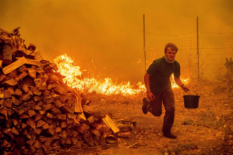Image: Alex Schenck carries a water bucket while fighting to save his home from the Ranch Fire