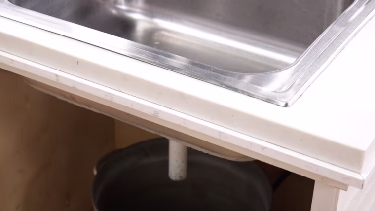 Hey, sometimes you just have to hack it! A metal bucket catches water and other liquids from this unplumbed sink.