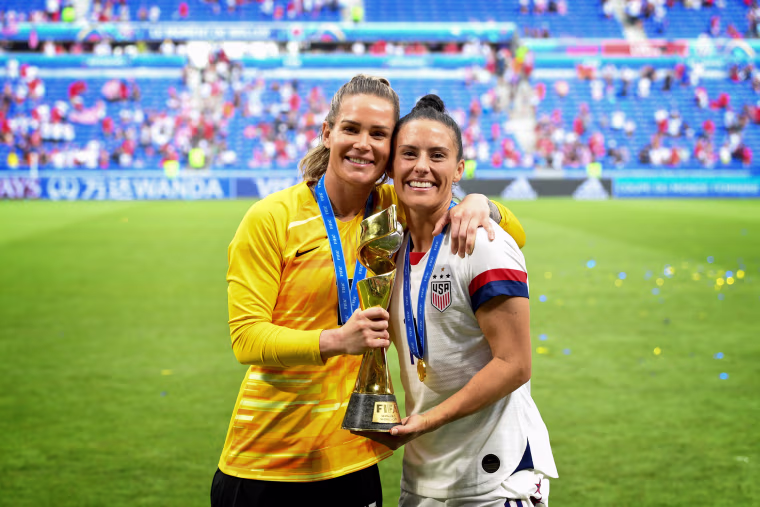 Image: Ashlyn Harris and Ali Krieger pose with the World Cup trophy after the United States defeated the Netherlands in the FIFA Women's World Cup on July 7, 2019.