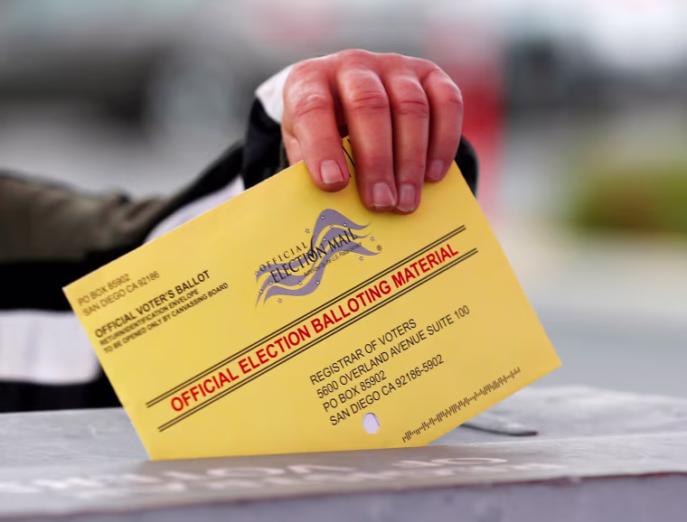 Image: A poll worker places a mail in ballot into a voting box as voters drop off their ballot in the U.S. presidential primary election in San Diego, California