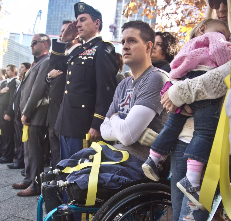 Former U.S. Air Force Senior Airman Brian Kolfage, center, sits in a wheelchair next to his wife Ashley, right, who holds their daughter Paris, during the National September 11 Memorial and Museum's "Salute to Service" tribute honoring U.S. veterans in New York on Nov. 10, 2014.