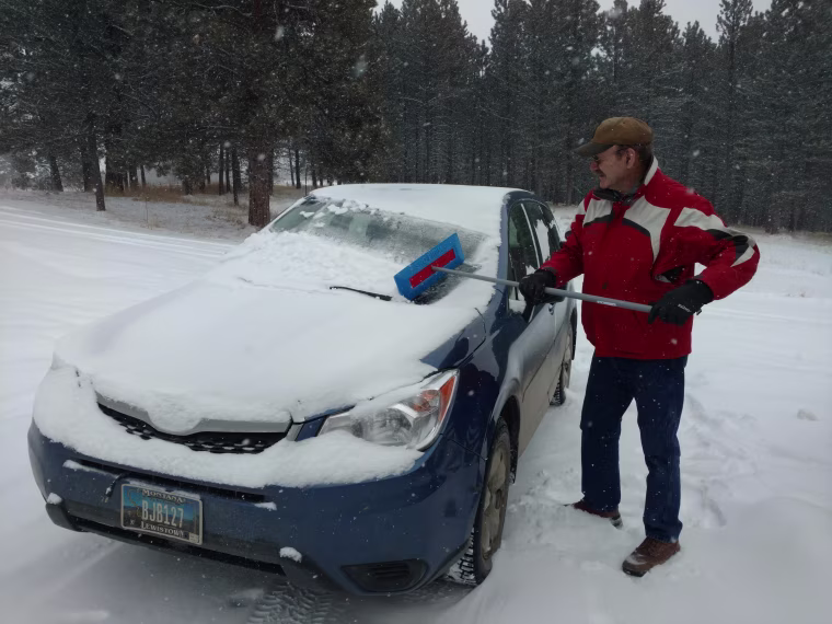 Mel Jackson cleaning snow off of his wife's Subaru Forester.