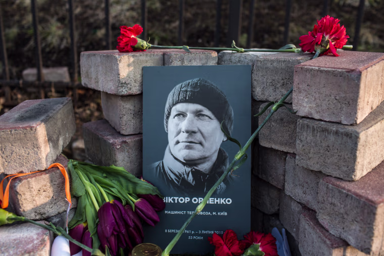 Image: A photograph of Viktor Orlenko is displayed at a makeshift memorial 