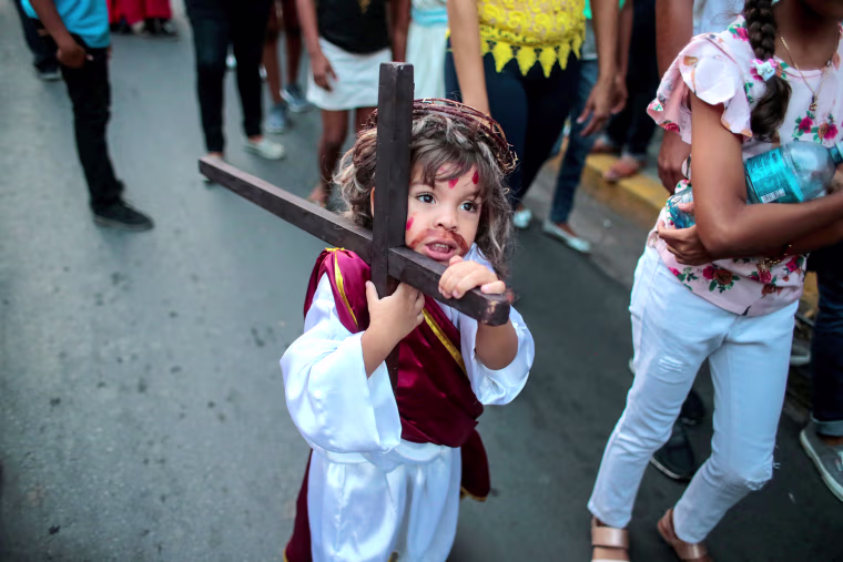 Image: A child dressed as Jesus Christ carries a wooden cross during the \"Jesus del gran poder\" procession in the colonial city of Granada