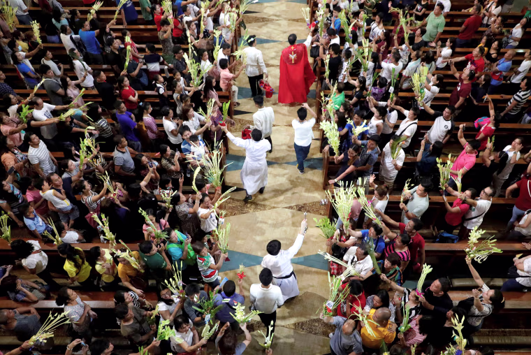 Image: A Catholic priest sprinkles holy water over palm fronds before Palm Sunday mass