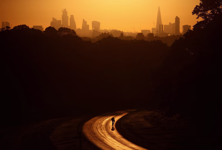 Image: The sun rises behind The Shard and the financial district as a cyclist rides through Richmond Park in London