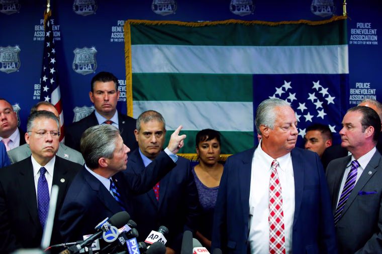 Image: NYPD Police Benevolent Association President Lynch points to the NYPD flag which is hanging upside down as a protest at a news conference in New York