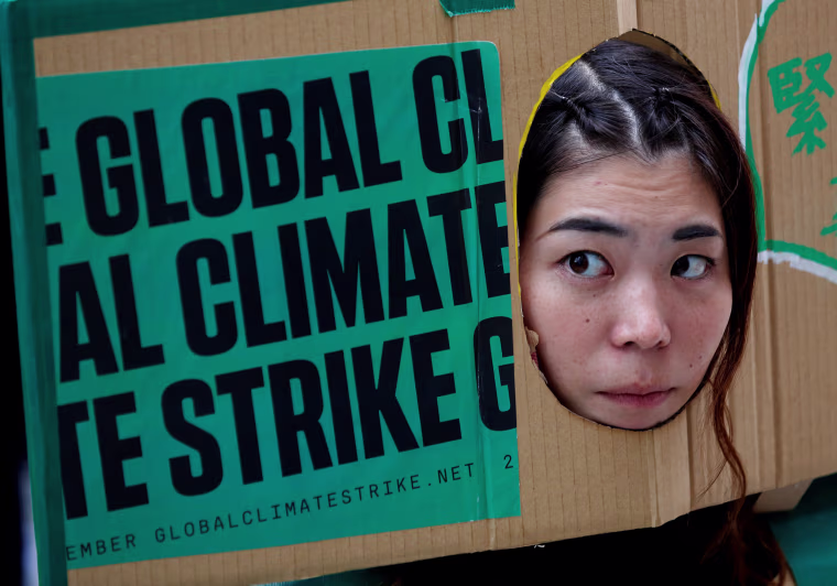 Image: A woman puts her face out of a banner at an event to mark the day of global climate strikes in Tokyo