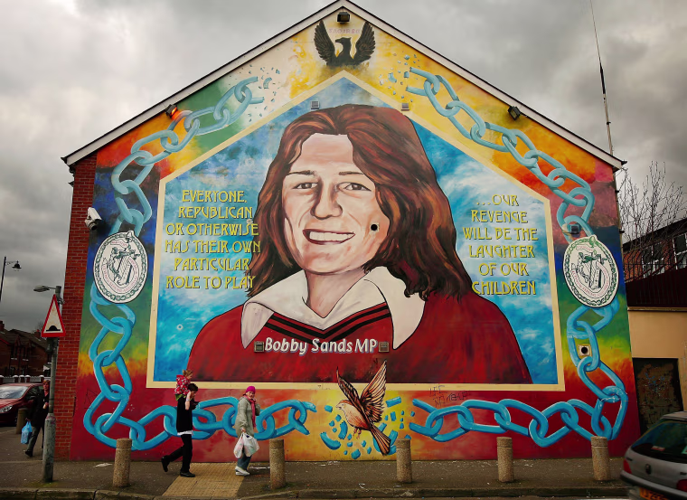 Image: A couple walks past a mural depicting Bobby Sands in the Falls Road on April 10, 2008, in Belfast.